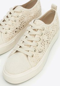 Beige Leinensneaker mit einem strukturierten Schnürdesign, flachen Baumwollschnürsenkeln und einer Gummisohle. Enthält metallische Ösen und eine verstärkte Zehenpartie.