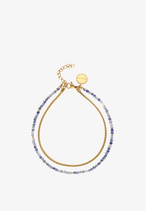 Pulsera de doble capa con pequeñas cuentas azules y blancas en una hebra y una cadena dorada en la otra, con un cierre dorado y una etiqueta redonda.