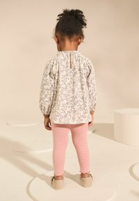 Romantisch crèmekleurig top met bloemenpatroon, met pofmouwen en een sleutelgatrug, gecombineerd met roze en witte gestreepte leggings en beige instappers.