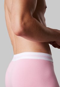 Boxer da uomo in cotone rosa con elastico bianco in vita che presenta un logo del brand discreto. Il tessuto ha un motivo testurizzato, mostrato di lato.