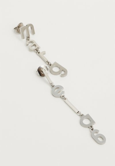 Metallörhänge med hängande bokstäver i en modern typografi, med en polerad silverfinish och en enkel kopplingsdesign.