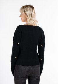 Maglione nero con scollatura ampia e maniche lunghe, con dettagli a forma di cuore dorati sulle maniche. Tessuto morbido e design aderente.