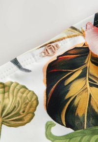 Bloemenstof met groene bladeren en oranje bloemen, met een opvallende ronde rosé gouden knop en nette stiksels langs de rand.