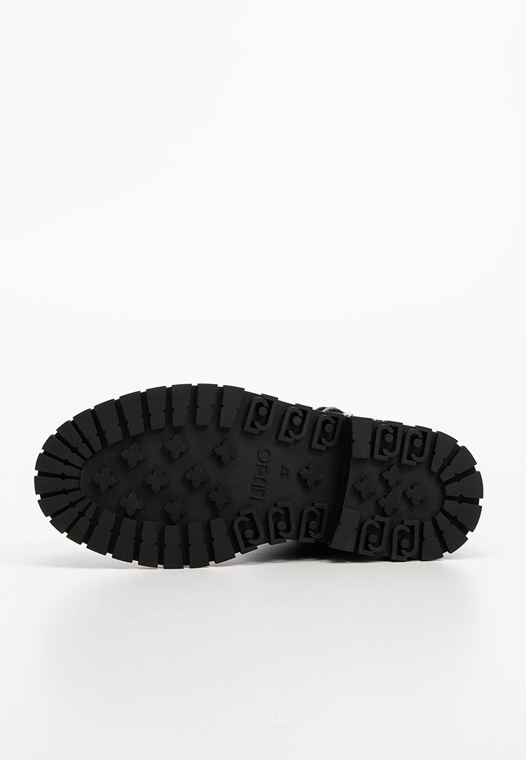 Schwarze Schuhsohle mit tiefen Profilen und rechteckigen, quadratischen sowie wirbelnden Mustern für Traktion, präsentiert vor einem weißen Hintergrund.