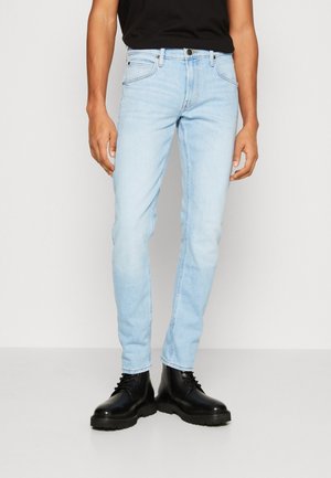 Dopasowane, jasnoniebieskie jeansy noszone z czarnymi, sznurowanymi butami i czarną koszulą, pokazane od talii do stóp na jednolitym tle.