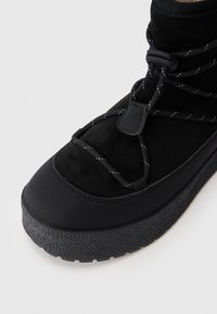 Zwarte winterlaarzen met een bovenwerk van suede, een gestructureerde rubberen zool en elastische veters. Het ontwerp omvat een gevoerde kraag voor comfort.