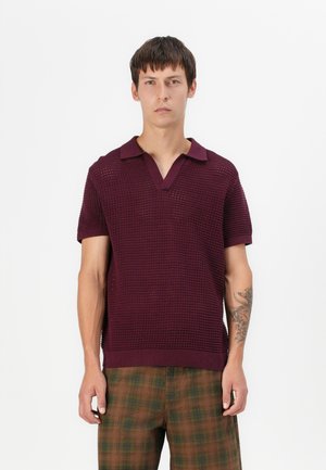Polo en tricot bordeaux avec un col en V et des manches courtes, associé à un pantalon à carreaux marron avec des accents verts et une coupe décontractée.