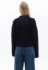 Maglione corto blu navy con texture a coste e colletto ampio, abbinato a jeans azzurri a vita alta con tasche posteriori.