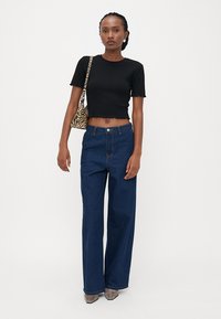 Schwarzes geripptes Crop-Top, hochgeschnittene weit geschnittene Jeans aus dunklem Denim, graue Absatzschuhe und eine Schultertasche mit Zebra-Muster. Einfacher und lässiger Look.