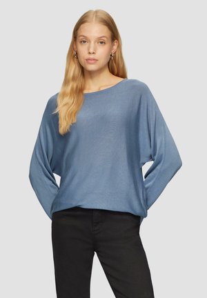 Lichtblauw, losvallend brei-topje met een wijde halslijn en lange mouwen. Zachte textuur en subtiele ribbels; gecombineerd met zwarte broek.
