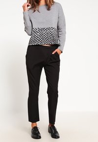 Maglia grigia a maniche lunghe con una sezione inferiore testurizzata e un motivo geometrico, abbinata a pantaloni neri a gamba affusolata e scarpe nere.