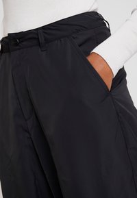 Svarta lätta byxor med en slät yta, med sidfickor, knäppning med knapp och en avslappnad passform. Enkelt design med minimal detaljering.