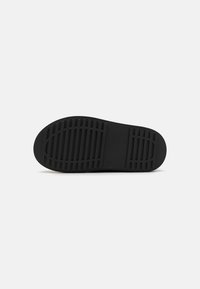 Semelle de chaussure en caoutchouc noir avec des motifs de traction texturés, présentant des rainures pour l'adhérence et un design plat et arrondi sans logos visibles.
