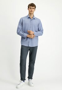 Jasnoniebieska koszula na guziki z małym wzorem w kratę, długie rękawy podwinięte na mankietach, zestawiona z ciemnoszarymi spodniami i białymi trampkami.