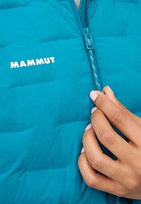Teal, isolerad pufferjacka med horisontell quiltad design, med en framzipper och en vit "MAMMUT"-logotyp på bröstet.
