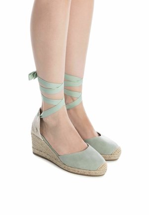 Sandalias de cuña espadrille en verde menta con tela suave, cintas en el tobillo y tacón de yute texturizado. Diseño de puntera redonda y espalda abierta.