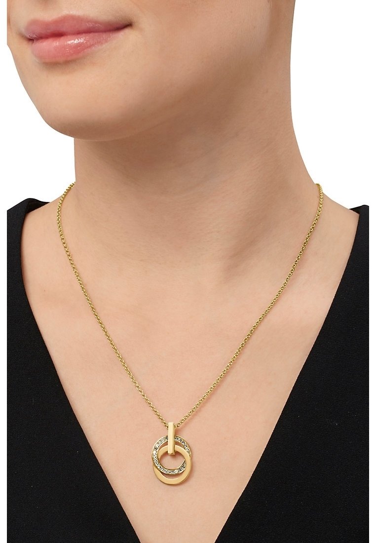 Personne portant une chaîne en or avec deux pendentifs circulaires entrelacés, un simple et un incrusté de petites pierres.