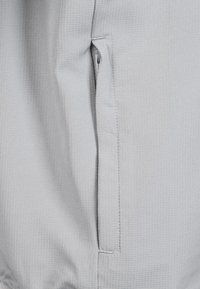 Tela gris con un patrón texturizado y acanalado, que incluye un bolsillo lateral con un zipper oculto. Costuras limpias a lo largo de los bordes.