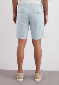 Shorts bleu clair en tissu texturé, dotés de deux poches arrière à bouton et d'une coupe droite. Coutures et détails d'ourlet visibles.