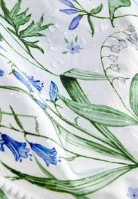 Tissu blanc avec des feuilles vertes et des motifs floraux bleus, couvert de gouttelettes d'eau.