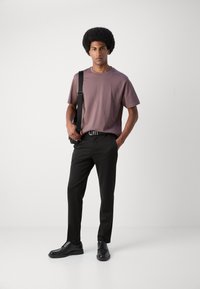 Tricou roz pal cu maneci scurte, asortat cu pantaloni negri eleganti si pantofi negri de birou, purtand o geanta pe umar.