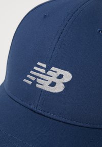 Cappello blu navy in tessuto testurizzato, con un logo ricamato bianco "NB" sul lato e dettagli di cucitura visibili.