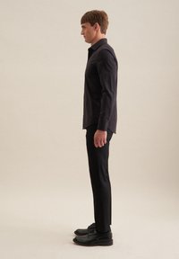 Camicia nera a maniche lunghe con una vestibilità slim e chiusura a bottoni, abbinata a pantaloni neri su misura e scarpe nere con lacci.