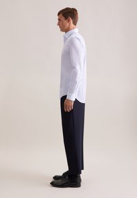 Shirt: lichtblauw, lange mouwen, slim fit met subtiele textuur. Broek: marineblauw, wijd gesneden. Schoenen: zwart, veterschoenen met een gladde afwerking.