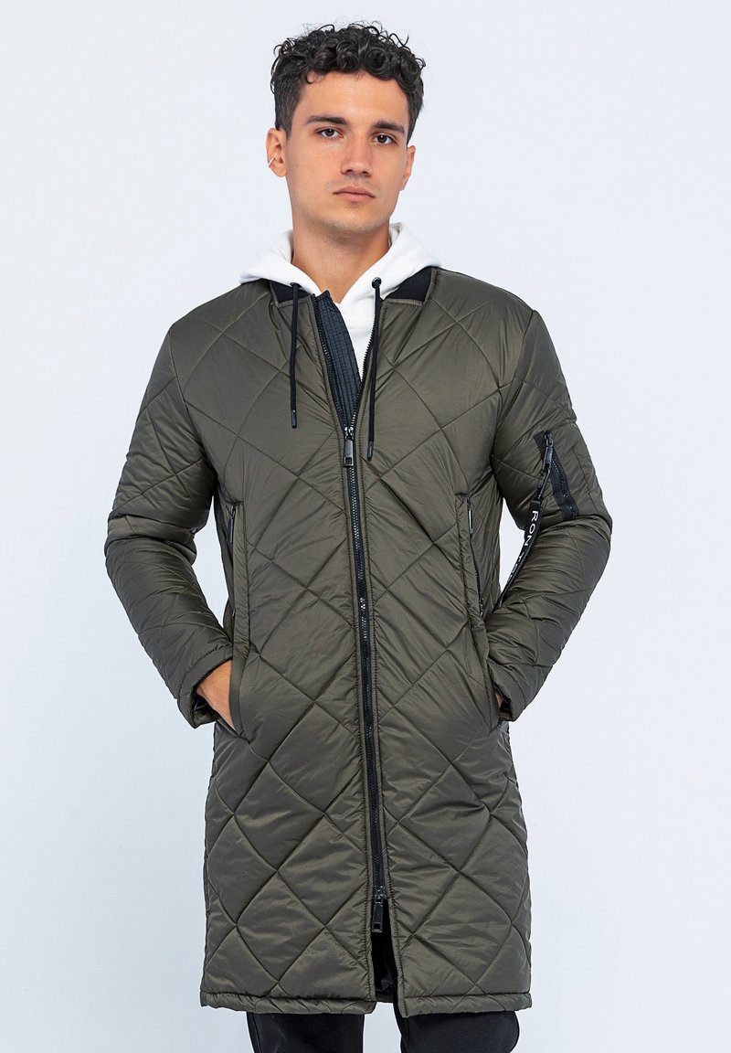 Gesteppten, langen olivgrünen Mantel mit Reißverschluss, schwarzen Akzenten und Seitentaschen. Besitzt eine Kapuze und ein strukturiertes Gewebe.