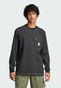 Long-sleeve black shirt with vertical white pinstripes, ribbed cuffs, and a chest pocket featuring a label. Textured fabric, casual fit.