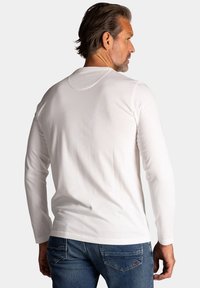 Wit t-shirt met lange mouwen van katoen, met een klassieke ronde hals en een nauwsluitend ontwerp, gecombineerd met blauwe denim jeans.