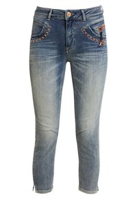 Jeans de denim azul con un diseño deslavado, que presentan tachuelas en tono cobre en los bolsillos frontales, un bolsillo con cremallera y aberturas en los tobillos.