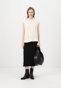 Ivory short-sleeve blouse with fringe trim, paired with a black pencil skirt and black heeled ankle boots, holding a black handbag.