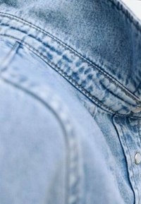 Giubbotto in denim azzurro chiaro con colletto, cuciture visibili e bottoni a pressione silver, che presenta una superficie texturizzata e un design casual.