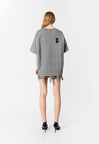 Top de tela gris de gran tamaño con mangas cortas, con costuras verticales, una etiqueta en la parte posterior y lazos en el dobladillo. Textura suave.