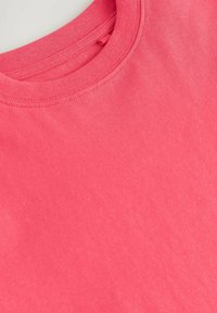 Kortærmet t-shirt med rund hals i lys koral, fremstillet af glat bomuldsmateriale med subtil tekstur, og med syningdetaljer langs halsudskæringen.