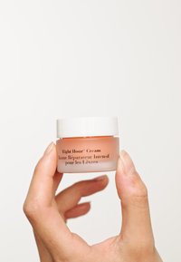 Balsamo labbra in un piccolo barattolo trasparente con coperchio bianco. Il barattolo contiene una crema morbida di colore pesca con testo nero sul lato.