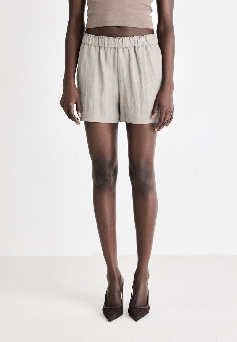 Light gray linen shorts with an elastic waistband, featuring a relaxed fit and minimal stitch detailing. Worn with brown pointed-toe heels.
