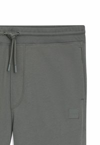 Gray sweatpants with a smooth texture, elastic waistband, drawstring ties, side pocket, and a small logo patch on the left thigh.