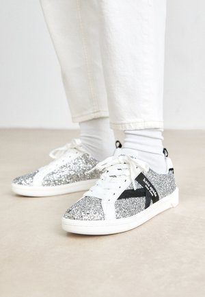 Sneakers argentati glitterati con un design bianco e nero. Presentano lacci e dettagli bianchi, e una superficie superiore testurizzata e scintillante.