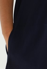 Navy blue garment with a smooth texture and a side pocket, featuring a clean design and minimalist stitching details.