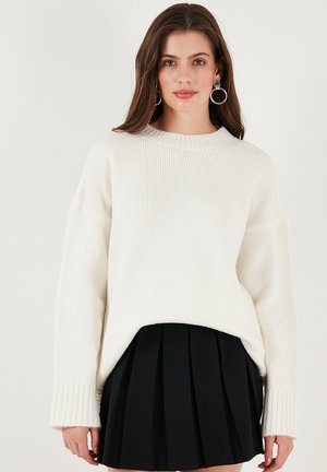 Weiße Strickjacke mit Rundhalsausschnitt, gerippten Bündchen und lockerer Passform, kombiniert mit einem schwarzen plissierten Rock.