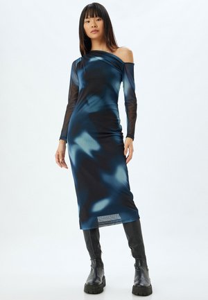 Robe à manches longues, décolletée, en bleu foncé avec des motifs abstraits clairs ; fabriquée en tissu lisse et extensible ; complétée par des bottes noires hautes jusqu'aux genoux.