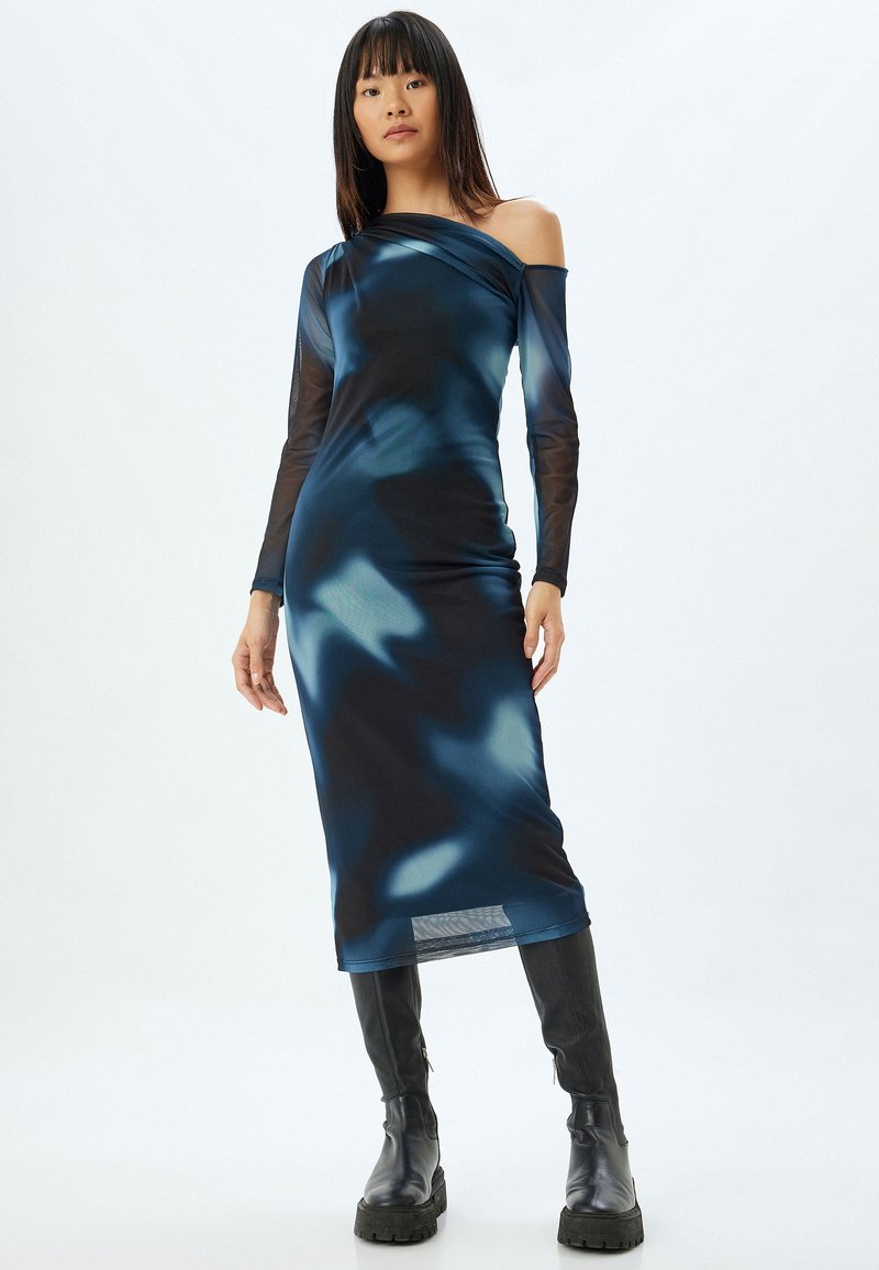Robe à manches longues, décolletée, en bleu foncé avec des motifs abstraits clairs ; fabriquée en tissu lisse et extensible ; complétée par des bottes noires hautes jusqu'aux genoux.