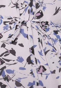Tecido lilás claro com um padrão floral em preto, azul e rosa; apresenta um detalhe de cintura amarrada e uma textura suave.