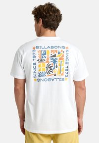 Bijela pamučna majica s višebojnim grafičkim dizajnom na leđima, ukrašena tropskim oblicima i natpisom "Billabong od 1973."