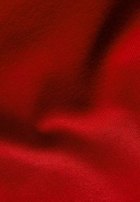 Tissu rouge lisse avec un motif discret de tissage diagonal et des plis doux créant des variations de lumière et d'ombre.
