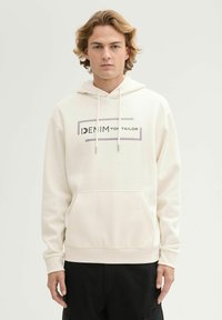 Crèmekleurige hoodie met een buidelzak, een capuchon met trekkoord en een grafisch "DENIM" logo in zwart en grijs gecentreerd op de voorkant. Zachte textuur.
