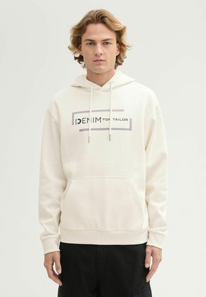 Hoodie crème avec une poche kangourou, capuche à cordon de serrage et logo graphique "DENIM" en noir et gris centré sur le devant. Texture douce.