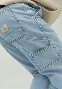 Ljust blå denimjeans med flera fickor, en texturerad yta och en liten etikett på bakfickan.